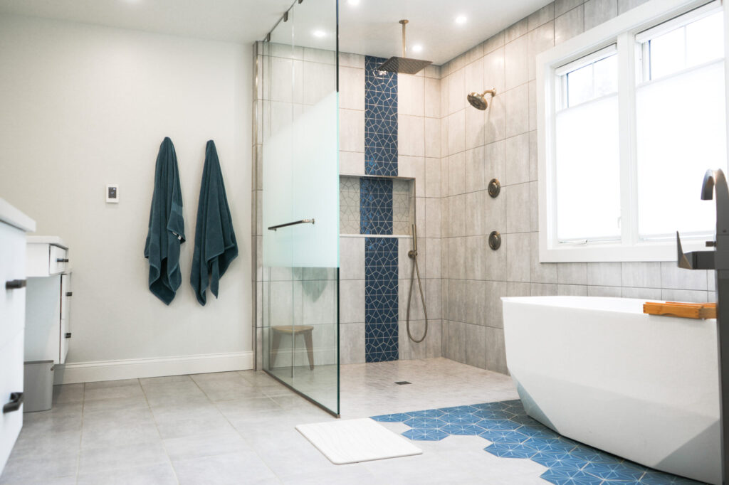 A modern walk-in shower with custom geometric tile and a soaker tub